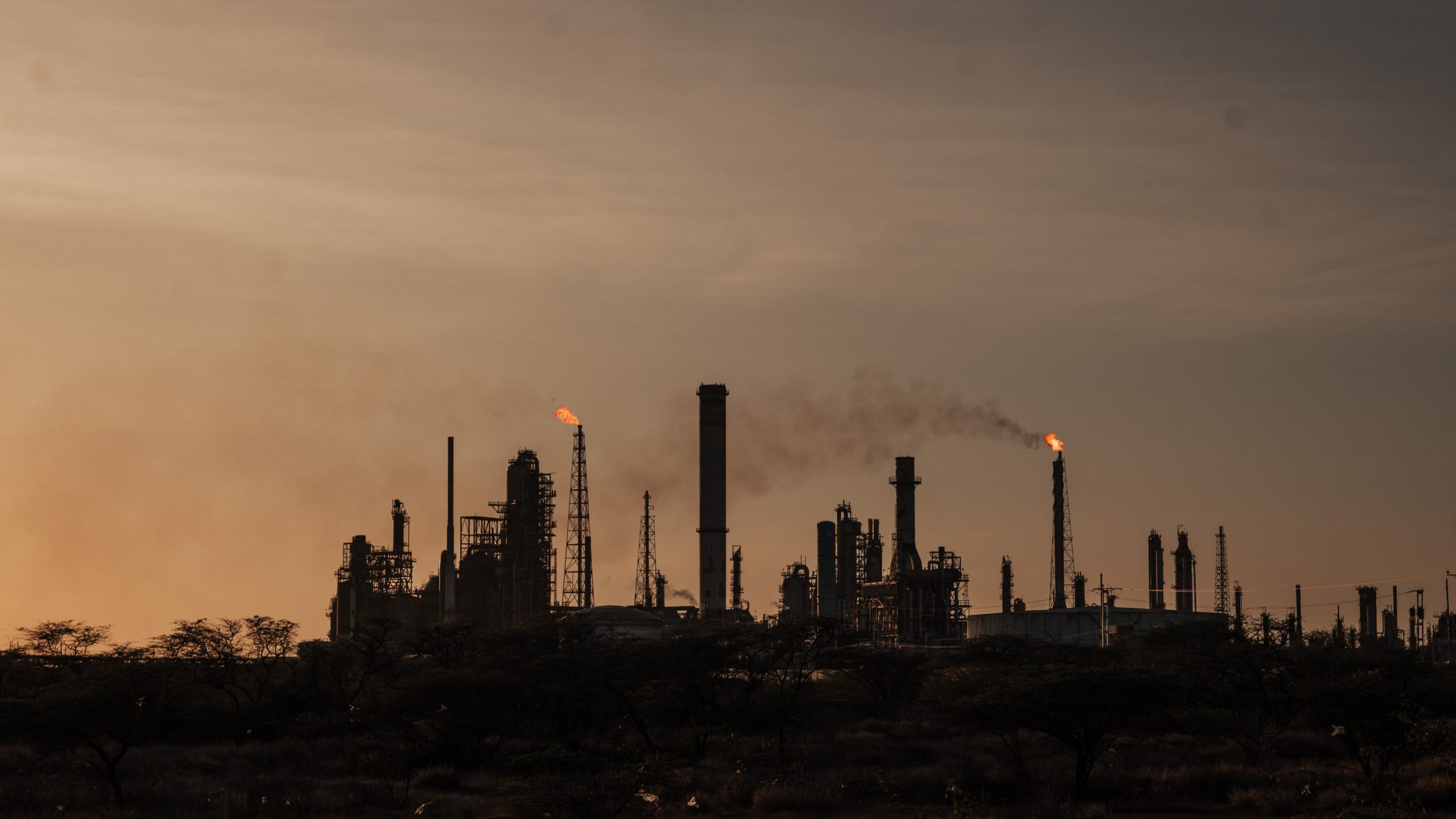 Un buque tanquero de grandes dimensiones en un puerto petrolero venezolano, con el sol de fondo y plataformas de carga de crudo.