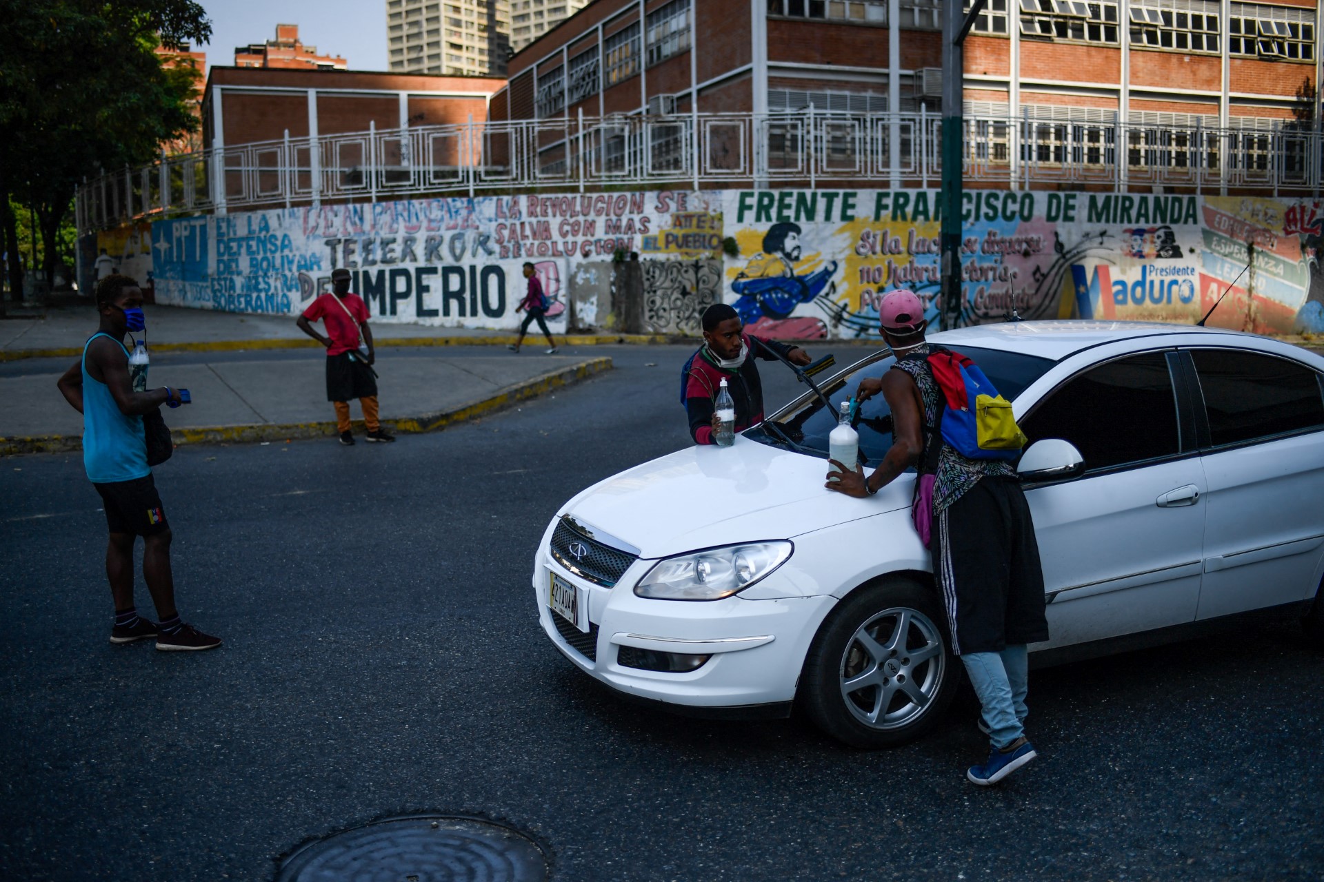 Grupo de jóvenes venezolanos con expresiones de preocupación, observando un edificio universitario con signos de deterioro en Venezuela.