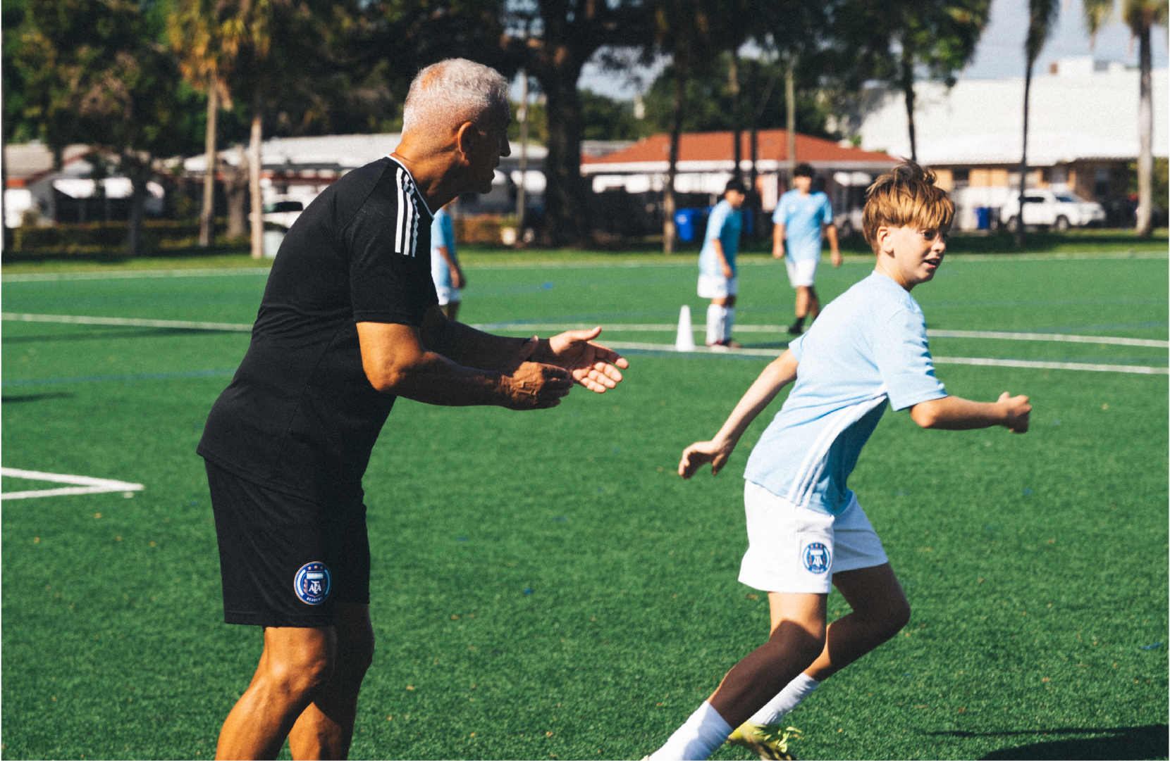 Jóvenes futbolistas entrenando en una cancha bajo la supervisión de entrenadores.