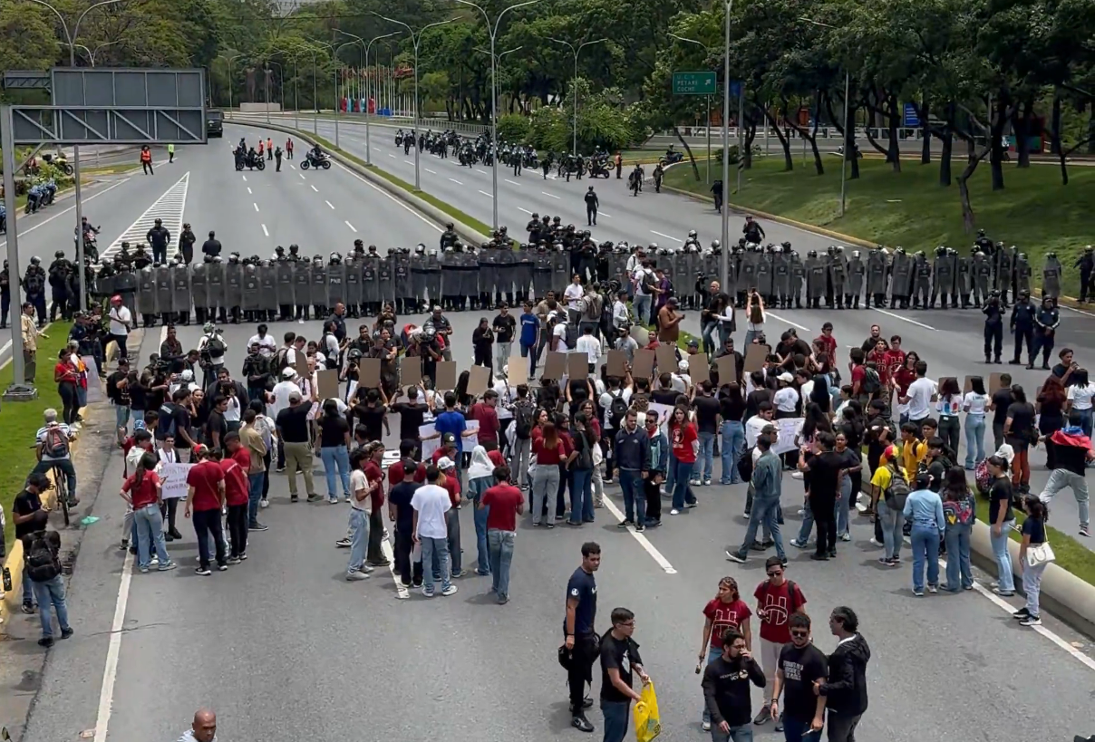 Estudiantes universitarios pintando un mensaje en el asfalto de la autopista Francisco Fajardo durante una protesta en Caracas.