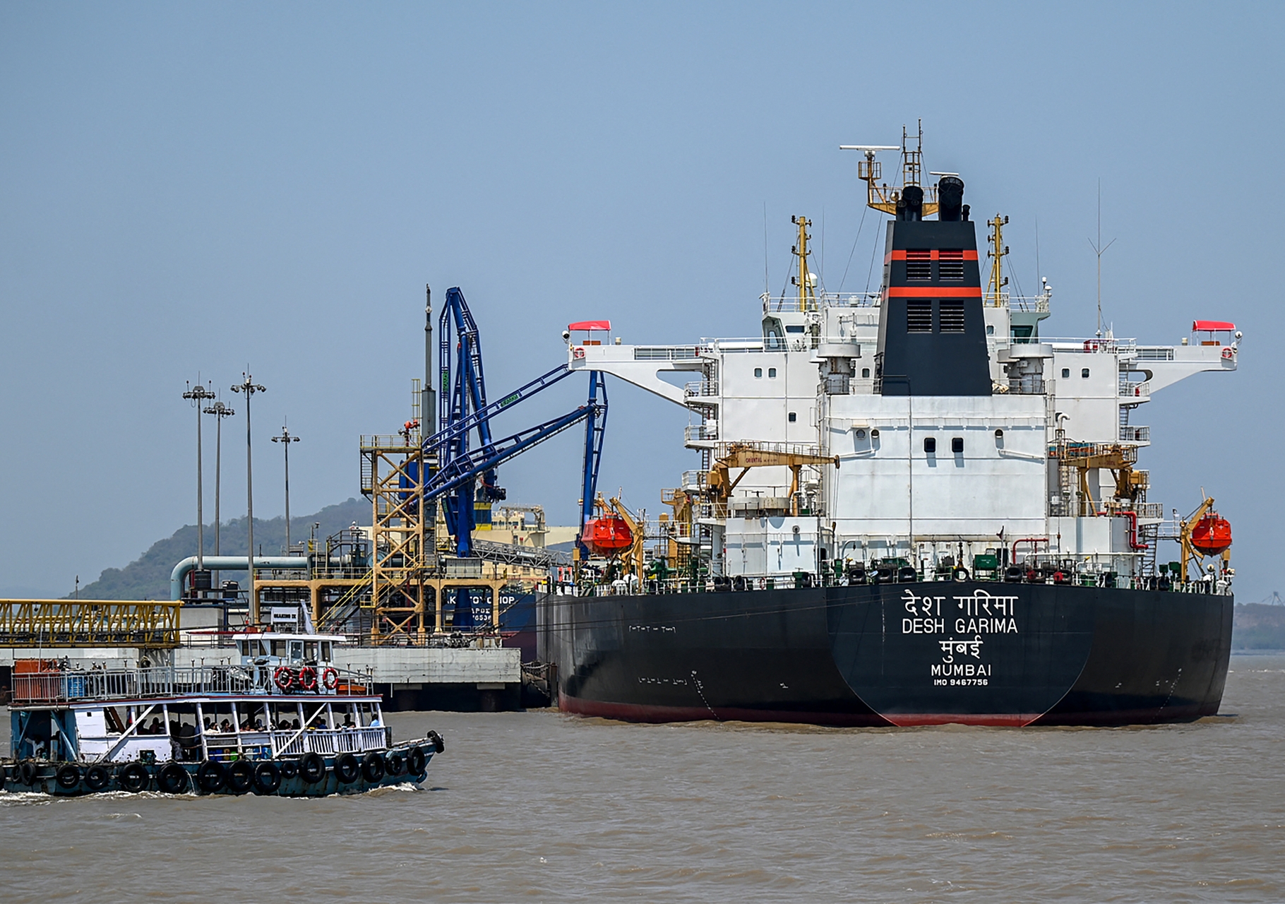 Vista aérea de una refinería de petróleo procesando crudo, con buques cisterna esperando en el mar.