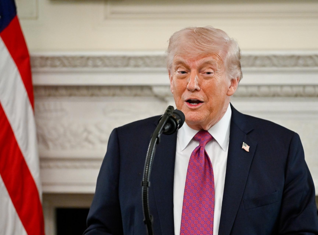 Donald Trump en un podio con banderas de Estados Unidos, haciendo una declaración sobre economía y petróleo.