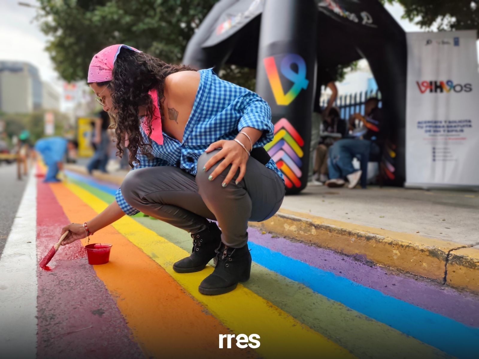 Personas repintando la ciclovía arcoíris en La Castellana, Caracas, con banderas LGBTIQ+ y globos.
