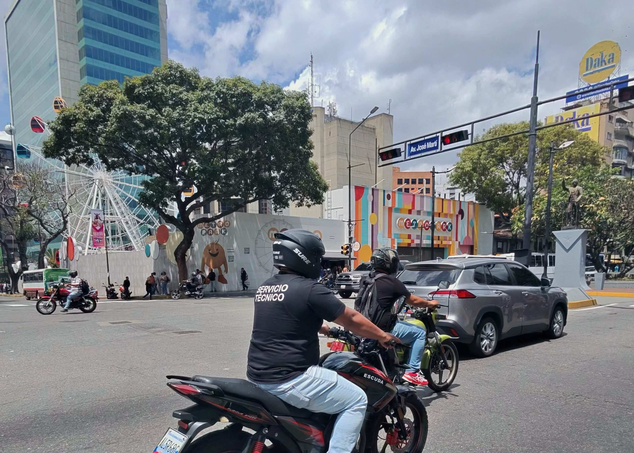 Mujeres venezolanas viajando como pasajeras en una motocicleta en una vía urbana.
