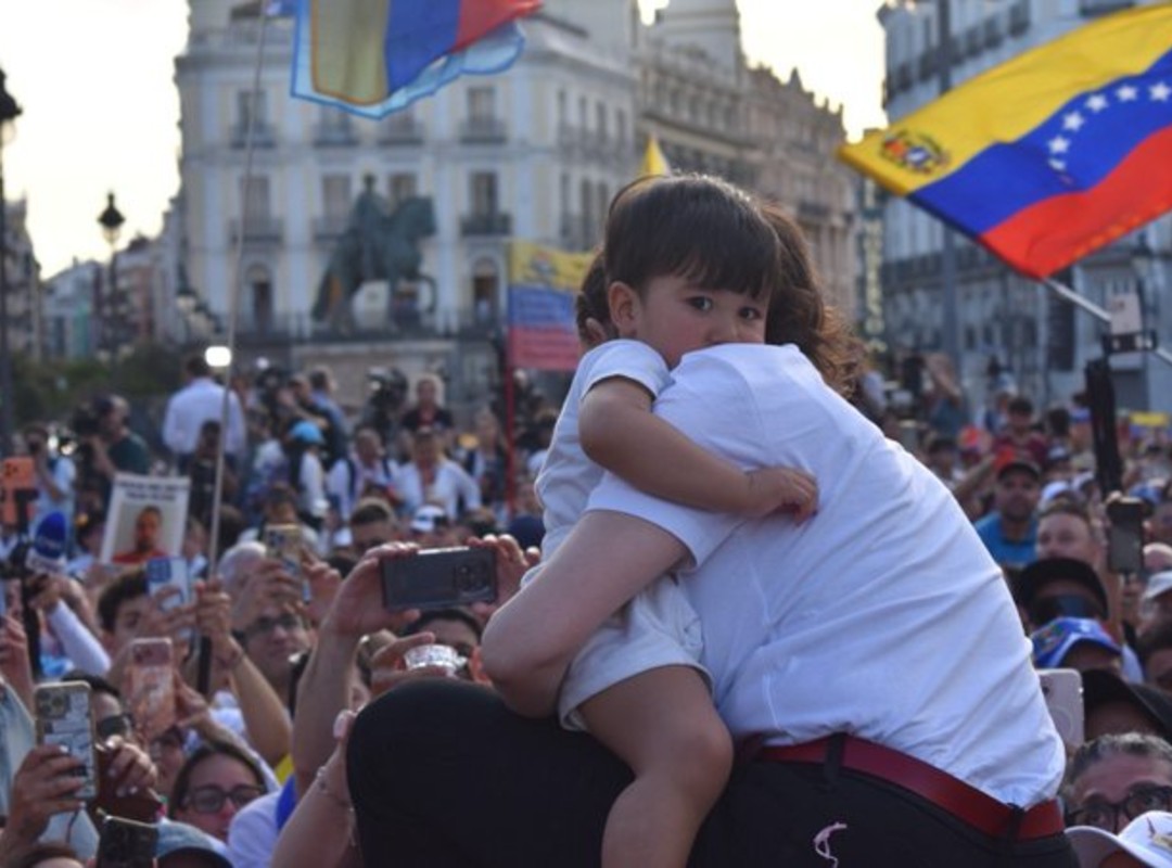 María Corina Machado dirigiéndose a una multitud, con banderas de Venezuela de fondo.