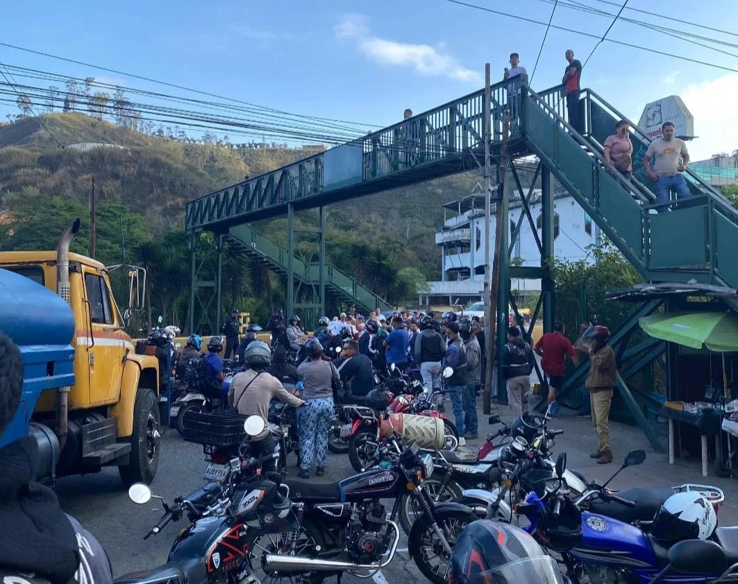 Personas protestando y bloqueando una carretera con vehículos y pancartas en Los Teques, Venezuela.