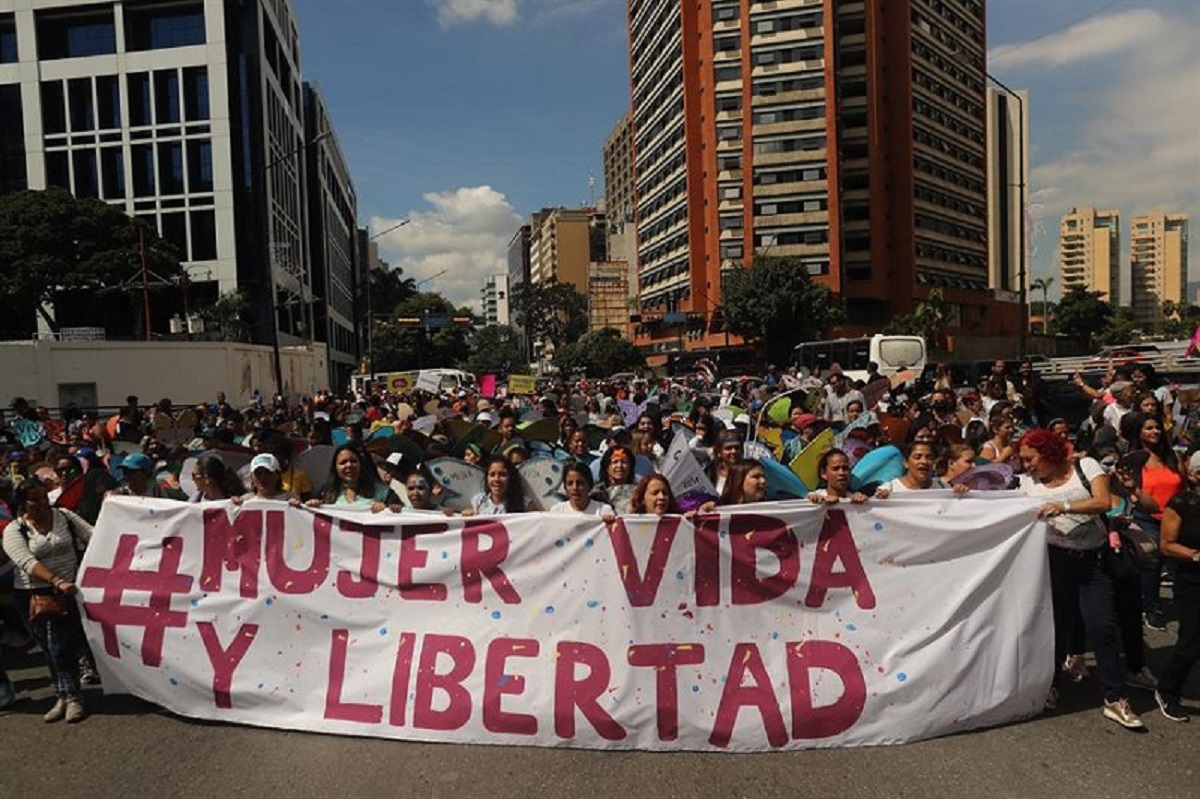 Ilustración de manos unidas en señal de apoyo contra la violencia de género, con un mapa de Venezuela al fondo.
