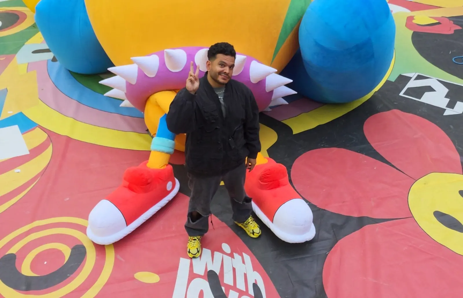 Luis Albornoz, artista gráfico venezolano, sonriendo frente a una de sus coloridas y llamativas creaciones artísticas.