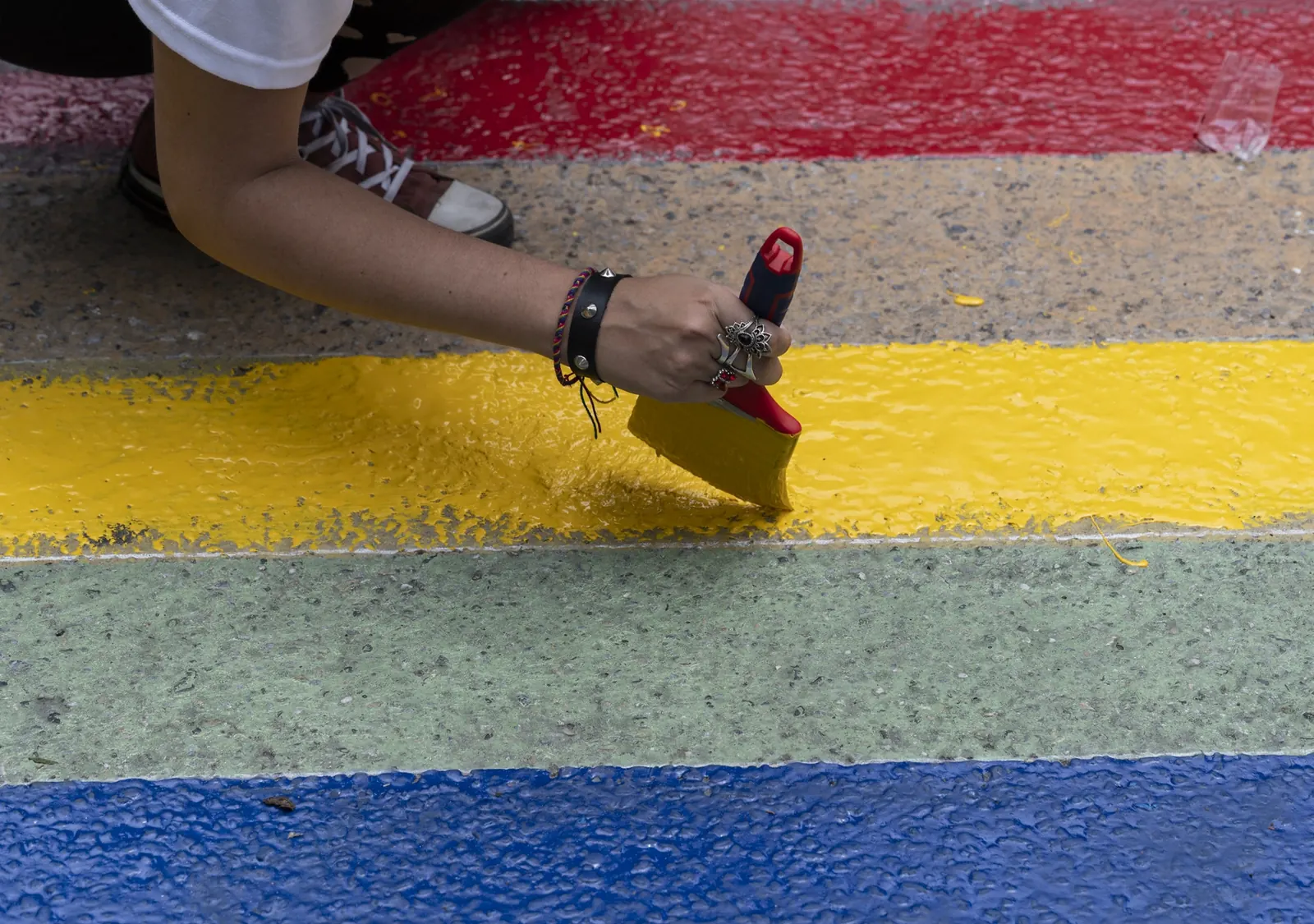 Un grupo diverso de personas LGBTIQ+ participa en una manifestación pacífica en una calle de Caracas, Venezuela, portando pancartas y ondeando banderas del arcoíris.