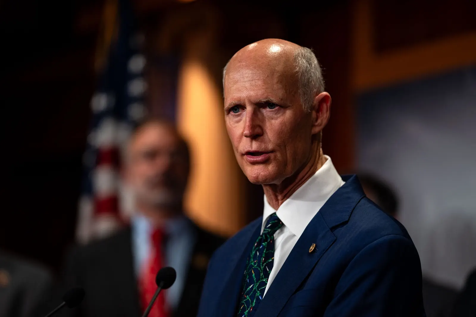 Senador Rick Scott durante una conferencia de prensa, con un micrófono frente a él.