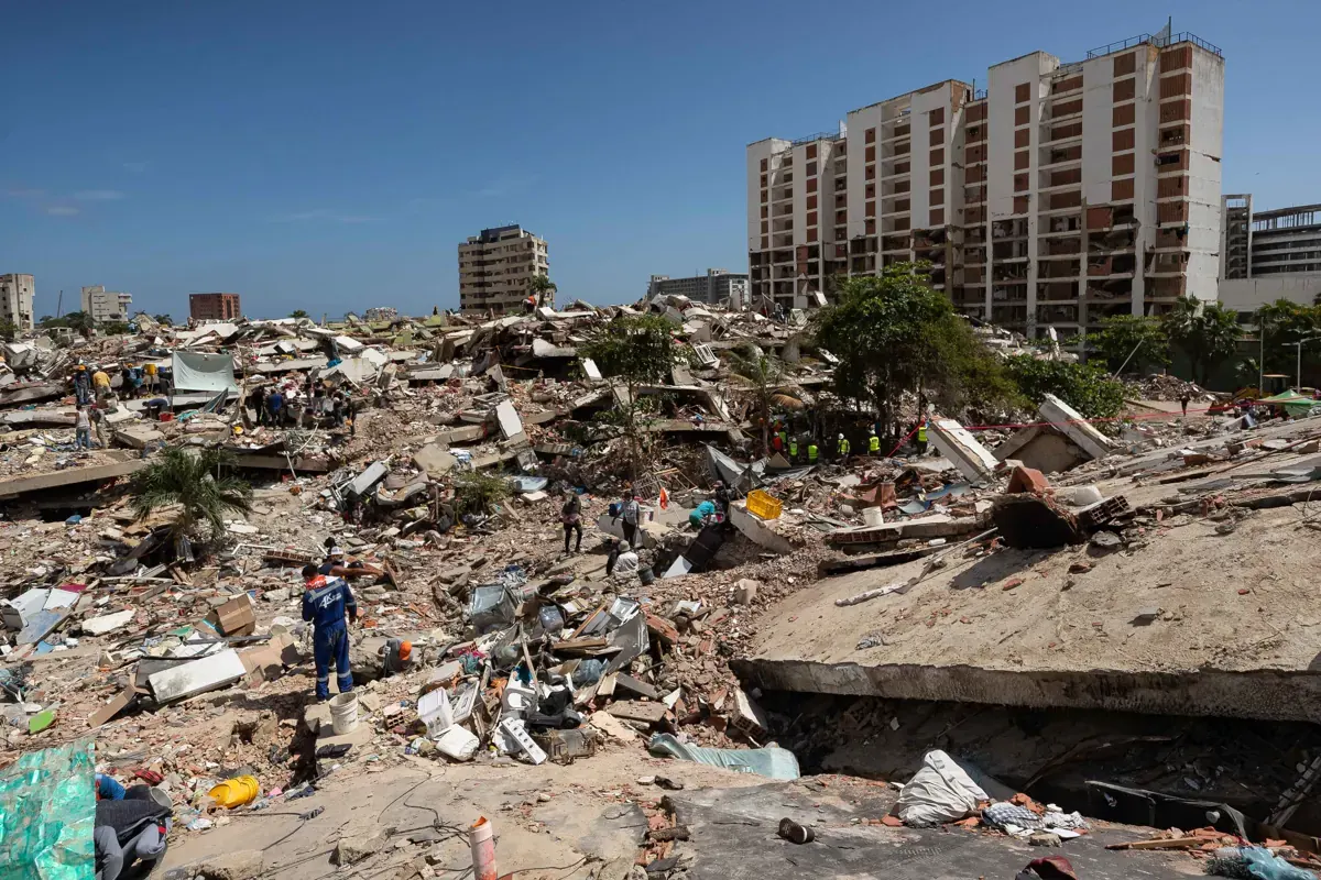 Ingenieros civiles con cascos y chalecos realizan inspecciones en la fachada de un edificio visiblemente afectado por un sismo, en una calle de Venezuela.