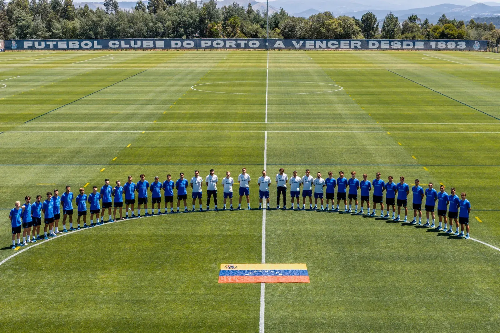 Jugadores del FC Porto en formación en el campo de entrenamiento, con una bandera venezolana en el césped, guardando un minuto de silencio.