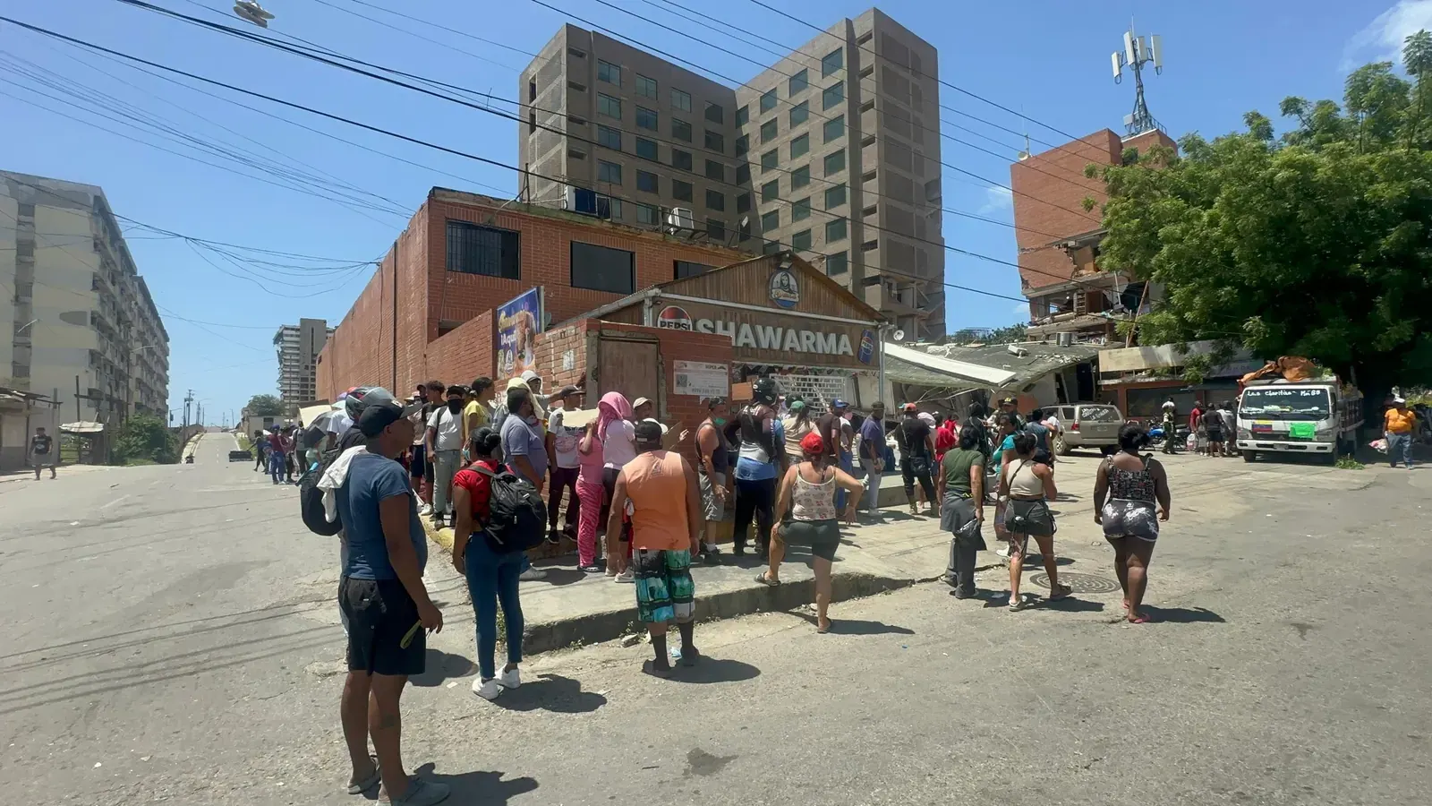 Comerciantes venezolanos reabren sus tiendas en La Guaira, mostrando productos y atendiendo a clientes en medio de edificaciones afectadas por un terremoto reciente.